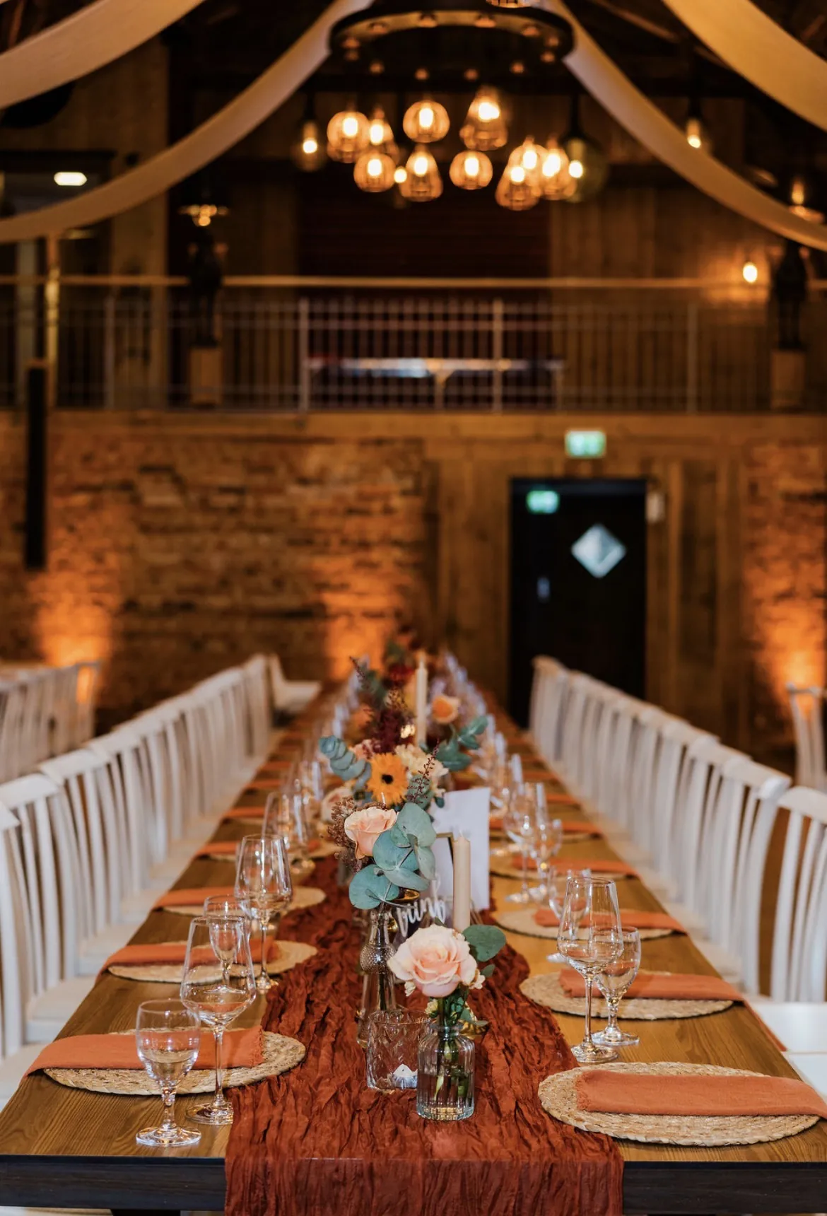 Lange Hochzeitstafel mit Tischläufer in Terrakotta, Blumen und Kronleuchtern
