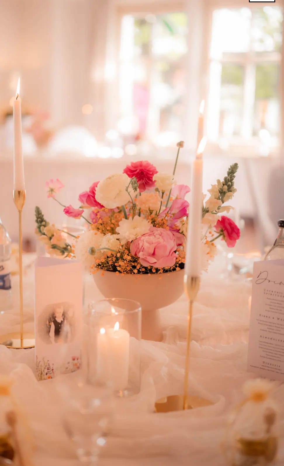 Tischdekoration mit pinken Blumen in Pokalvase und hohen Kerzen